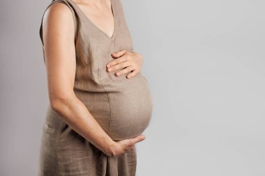 Hamile bir kadın arka planda durarak karnına dokunuyor. Hamilelik, beklenti, annelik kavramı.
