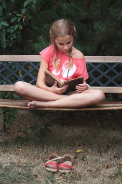 Girl reading a book on a bench in the park