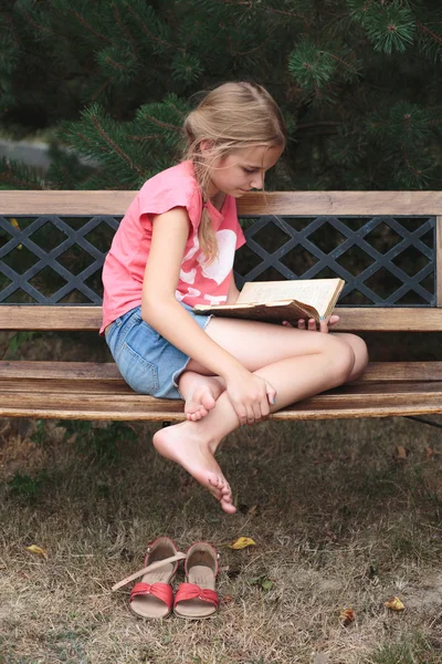 Mädchen liest ein Buch auf einer Bank im Park — Stockfoto