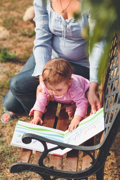 妈妈抱着小婴儿看一本书与图片 — 图库照片