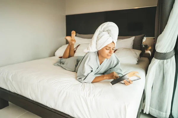 stock image Woman after shower laying on the bed and reading a book