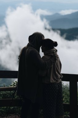Birbirine aşık çiftler, dağların ve bulutların muhteşem manzarasının zirvesinde dururlar.