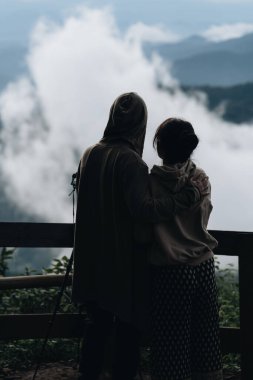 Birbirine aşık çiftler, dağların ve bulutların muhteşem manzarasının zirvesinde dururlar.