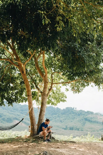 Człowiek Siedzi Pod Drzewem Kontroluje Drona Tajlandia — Zdjęcie stockowe