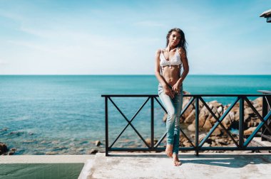 Kumsaldaki villada duran kot pantolon ve beyaz bluz giyen çekici genç manken.