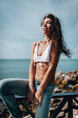 Kumsaldaki villada duran kot pantolon ve beyaz bluz giyen çekici genç manken.