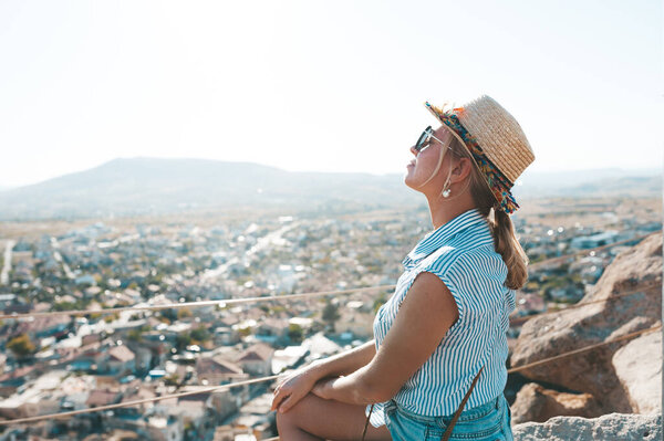Woman sitting at the edge and enjoyng amazing view from Uchisar Castle in Cappadocia.