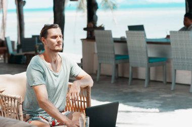 Plajda dizüstü bilgisayarla çalışan serbest çalışan bir adam.