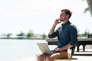 Plajda dizüstü bilgisayarla çalışan serbest çalışan bir adam.