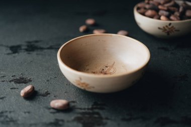 Koyu arkaplanda küçük kase ve kakao çekirdeği.