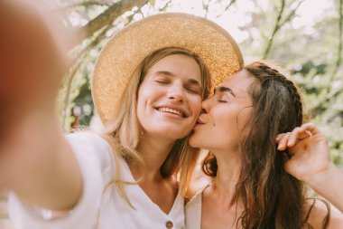 İki mutlu kız selfie çekiyor ve öpüşüyor.