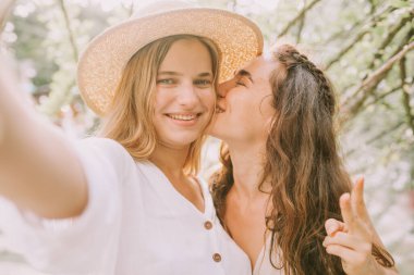İki mutlu kız selfie çekiyor ve öpüşüyor.