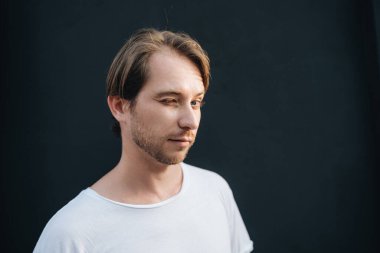 Koyu duvar arka planında beyaz tişörtlü Avrupalı göz kırpan adamın portresi