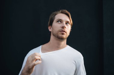 Avrupalı beyaz tişörtlü mutlu bir adamın portresi koyu renk arka planda sıcak basıyor.