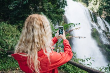Kırmızı ceketli bir kadın Tayland 'da Wachirathan şelalesinin fotoğrafını çeker.