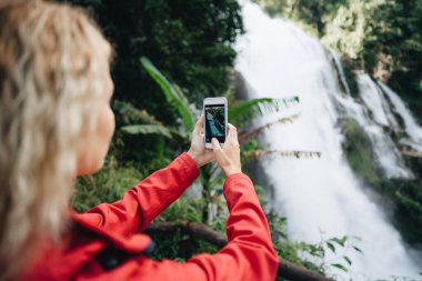 Kırmızı ceketli bir kadın Tayland 'da Wachirathan şelalesinin fotoğrafını çeker.