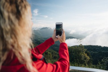 Kırmızı ceket giyen bir kadın Tayland 'ın en yüksek noktasındaki muhteşem manzaranın fotoğrafını çeker. Tayland 'ın en yüksek noktası Doi Inthanon