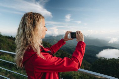 Kırmızı ceket giyen bir kadın Tayland 'ın en yüksek noktasındaki muhteşem manzaranın fotoğrafını çeker. Tayland 'ın en yüksek noktası Doi Inthanon