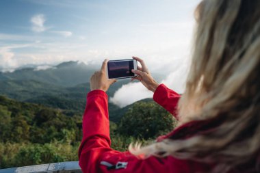 Kırmızı ceket giyen bir kadın Tayland 'ın en yüksek noktasındaki muhteşem manzaranın fotoğrafını çeker. Tayland 'ın en yüksek noktası Doi Inthanon
