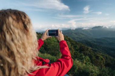 Kırmızı ceket giyen bir kadın Tayland 'ın en yüksek noktasındaki muhteşem manzaranın fotoğrafını çeker. Tayland 'ın en yüksek noktası Doi Inthanon