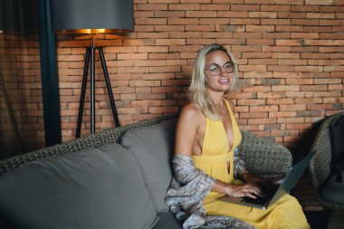 Genç bayan serbest yazar kanepede oturuyor kahve dükkanında dizüstü bilgisayarda çalışıyor.