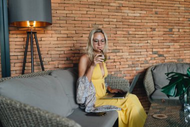 Genç bayan serbest yazar kanepede oturuyor kahve dükkanında dizüstü bilgisayarda çalışıyor.