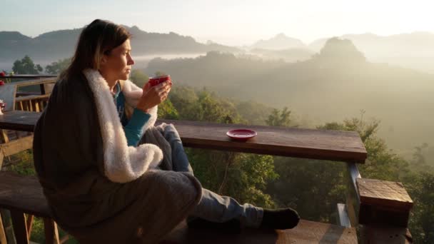 Kadın bir kafede oturuyor ve güneşin doğuşuyla Tayland 'ın kuzeyindeki dağlarda bir fincan kahve içiyor. — Stok video