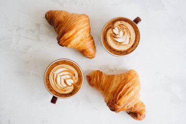 İki bardak cappuccino ve iki ay çöreği beyaz masada.
