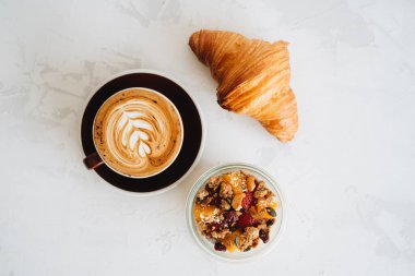 Bir fincan kahve, kruvasan ve puding beyaz masada.