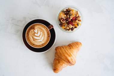 Bir fincan kahve, kruvasan ve puding beyaz masada.