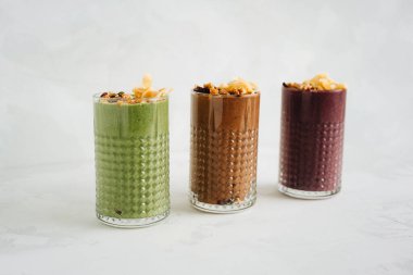 Beyaz zemin üzerinde granola olan üç farklı smoothie.