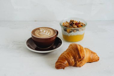 Durgun bir fincan kahve, kruvasan ve chia pudingi beyaz masada.