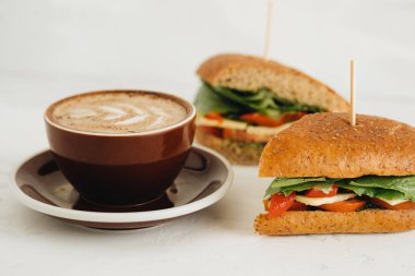 Bir fincan kahve ve panini 'nin durgun hayatı beyaz masada.