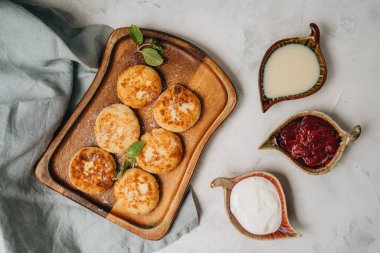 Syrniki beyaz bir masada tatlı süt ve reçelle servis edilir. Üst görünüm
