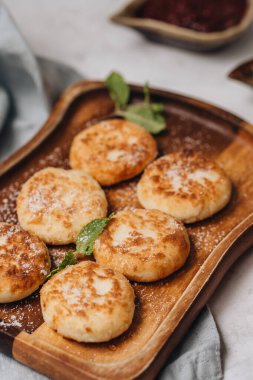 Syrniki beyaz bir masada tatlı süt ve reçelle servis edilir. Yan görünüm