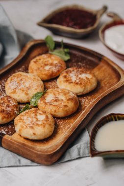 Syrniki beyaz bir masada tatlı süt ve reçelle servis edilir. Yan görünüm