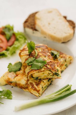 Beyaz tabakta domatesli omlet, ekmek ve kişniş. Yakın plan.