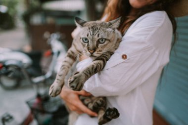 Dışarıda kediyi tutan şapkalı gülen bir kadın.