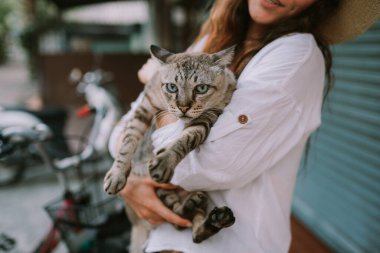 Dışarıda kediyi tutan şapkalı gülen bir kadın.