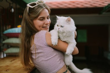 Dışarıda kediyi tutan şapkalı gülen bir kadın.