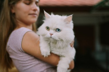Dışarıda kediyi tutan şapkalı gülen bir kadın.