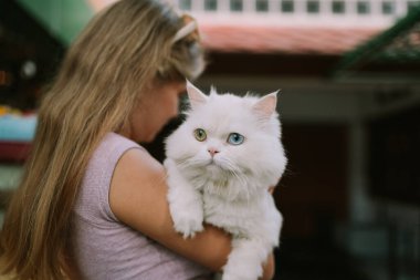 Dışarıda kediyi tutan şapkalı gülen bir kadın.