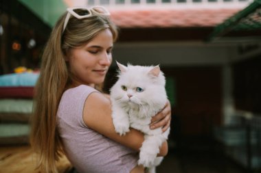 Dışarıda kediyi tutan şapkalı gülen bir kadın.