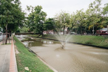 Fıskiyeleri, büyük ağaçları ve kıyılarında caddeleri olan bir kanalı izleyin. Chiang Mai, Tayland.