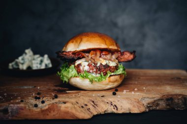 Beef burger with sauerkraut, pickles and mustard on wooden board and dark background