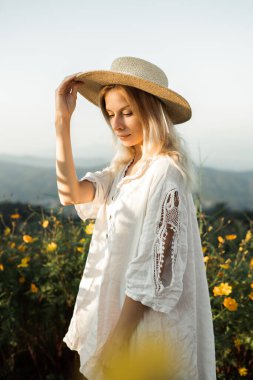 Mon Jam 'deki dağlarda çiçek tarlasında yürüyen, hasır şapkalı bir kadın.