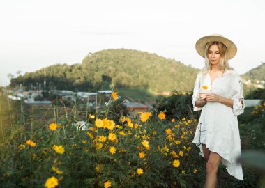 Mon Jam 'deki dağlarda çiçek tarlasında yürüyen, hasır şapkalı bir kadın.