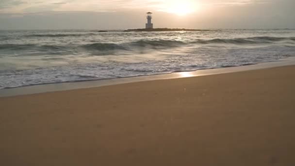 Αμμώδες τοπίο στην παραλία το ηλιοβασίλεμα. Κύματα στη θάλασσα. Φάρος — Αρχείο Βίντεο