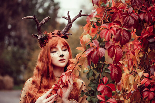 fairy woman with deer horns in autumn forest. Face painting. Beautiful mystery woman. redhead girl with big eyes magical sight