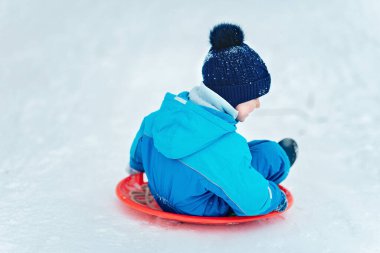 Çocuk bir kar tepesinden yuvarlanıyor. Çocuk kışın kar tepesinden aşağı kayıyor. Çocuklar dışarıda oynuyor. Kış eğlencesi.